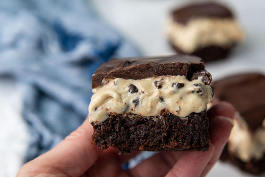 a hand holding up a cookie dough brownie close to the camera