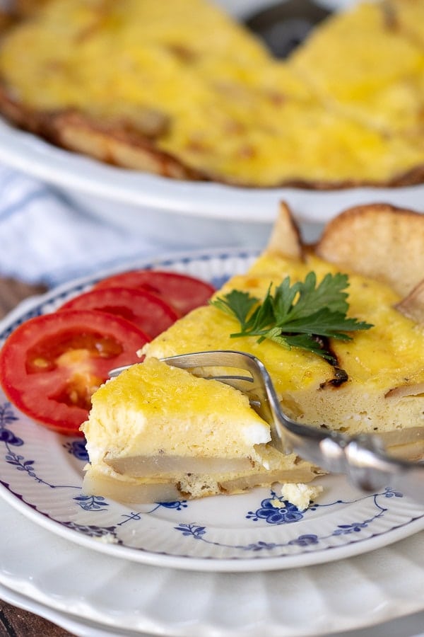 a fork cutting into a bite of potato frittata with sliced tomatoes resting next to it