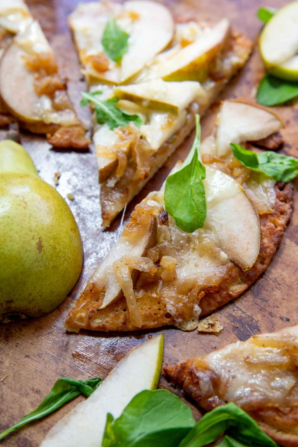 a slice of socca pizza with a sliced pear next to it