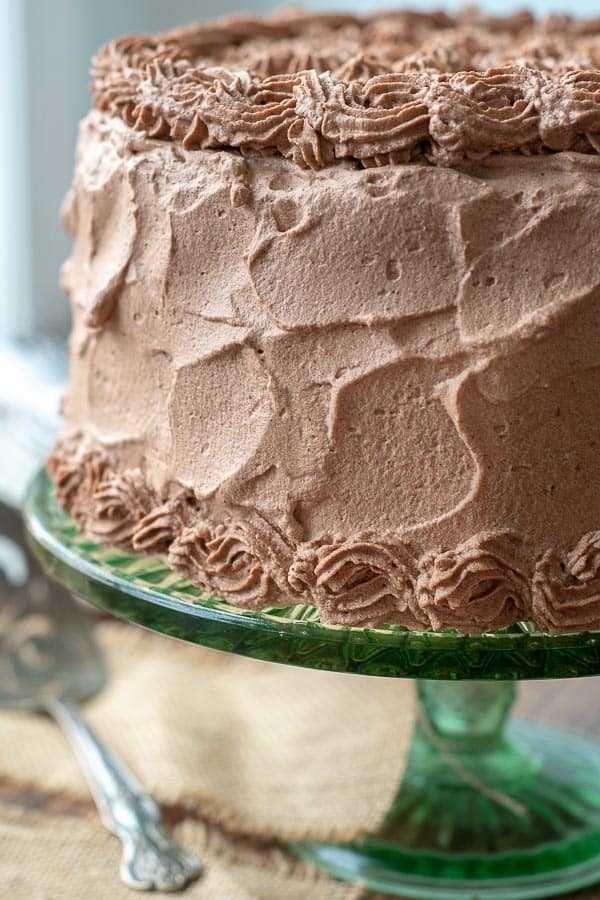 a banana cake on a green cake stand with chocolate whipped cream frosting all over it
