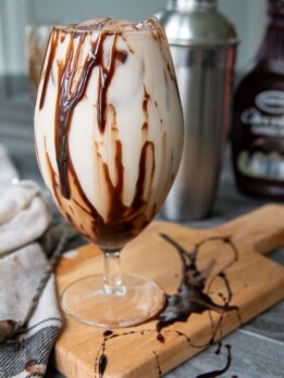 a colorado bulldog drink sitting on a wooden cutting board with chocolate syrup drizzled on glass