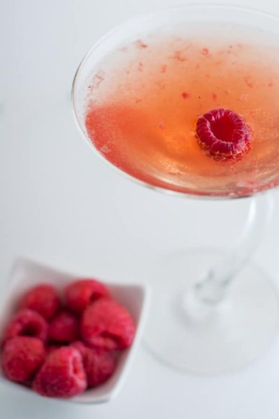 close up of raspberry martini cocktail with a bowl of fresh raspberries next to it
