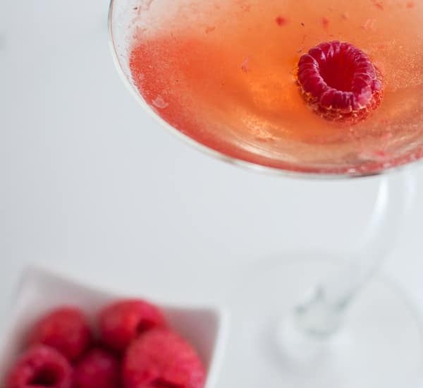 close up of raspberry martini cocktail with a bowl of fresh raspberries next to it