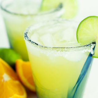 two glasses of skinny margarita with sliced oranges and limes lying next to them