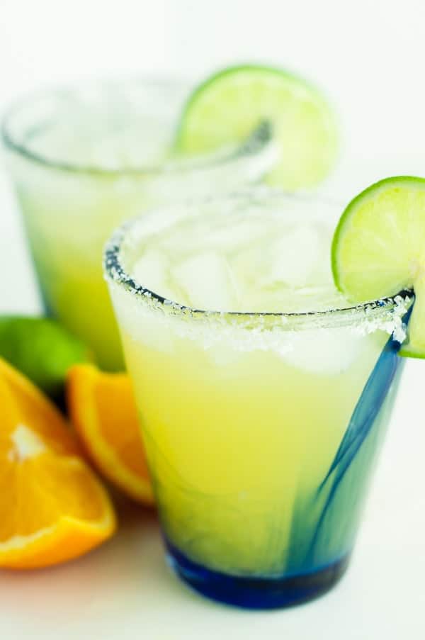 two glasses of skinny margarita with sliced oranges and limes lying next to them