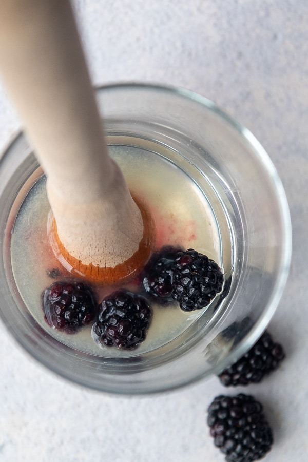 overhead shot of fresh blackberries being muddled in a glass