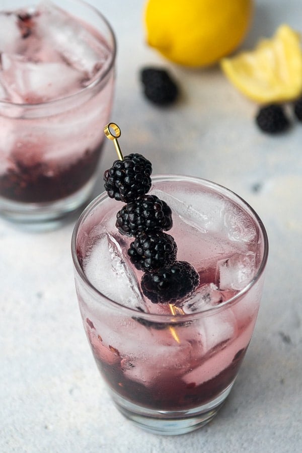 two blackberry vodka cocktails with freshly squeezed lemons in the background