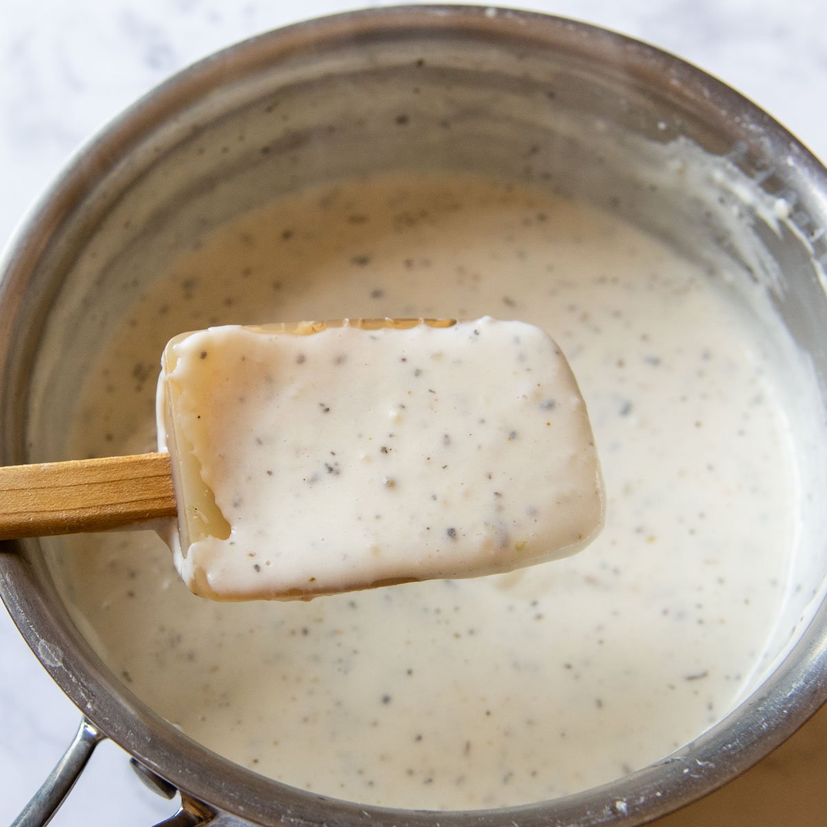 a spoon lifting out thickened white sauce.
