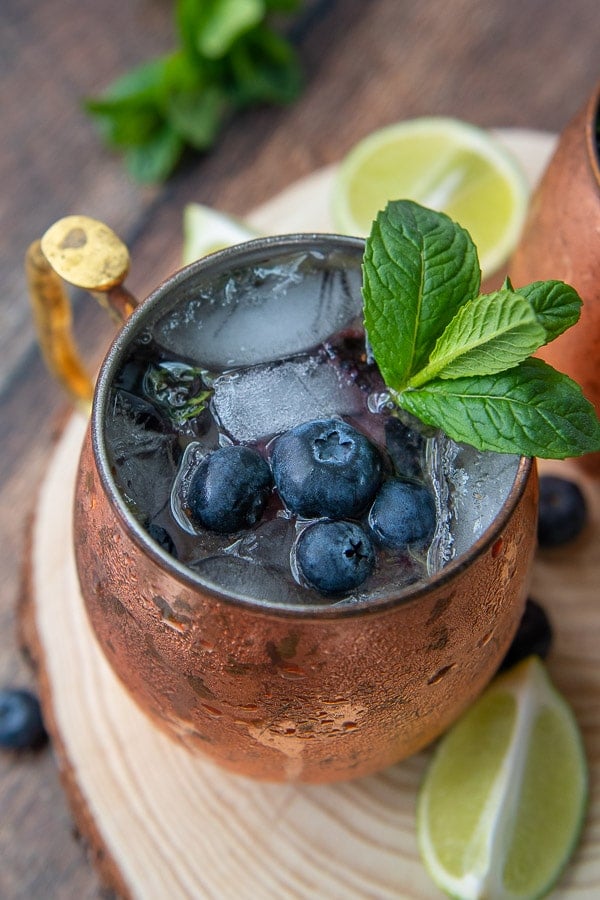 a side angle shot of blueberry moscow mule with fresh lime wedges laying next to it