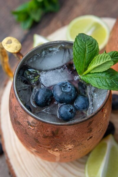 a side angle shot of blueberry moscow mule with fresh lime wedges laying next to it