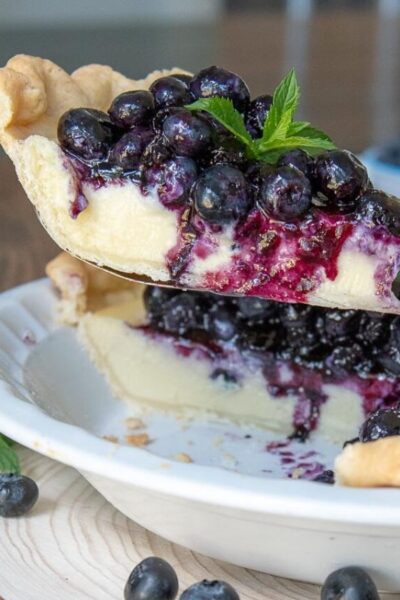 a pie server lifting a slice of blueberry cream pie out of a pie dish