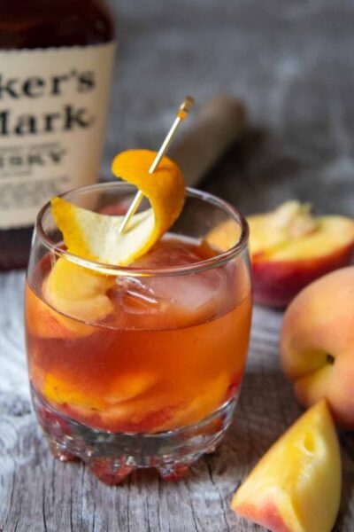 a peach old fashioned on a wood board with bourbon in the background