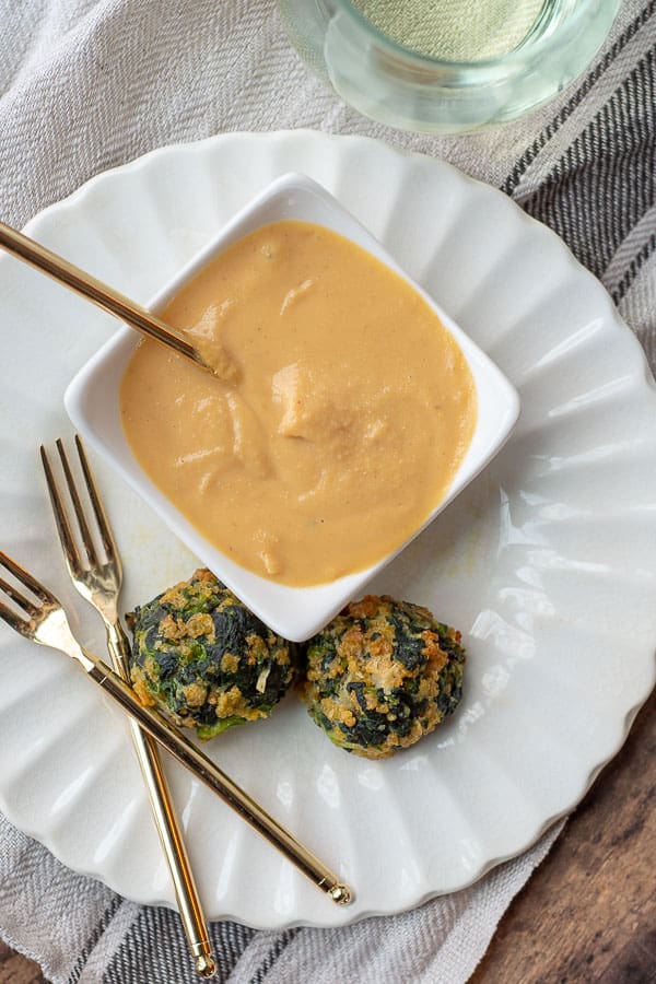 two spinach balls on a white plate with gold forks next to it