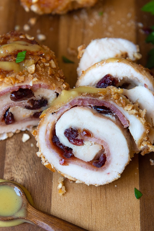 a slice of spiral rolled chicken on a wooden board with bacon and cranberries stuffed inside
