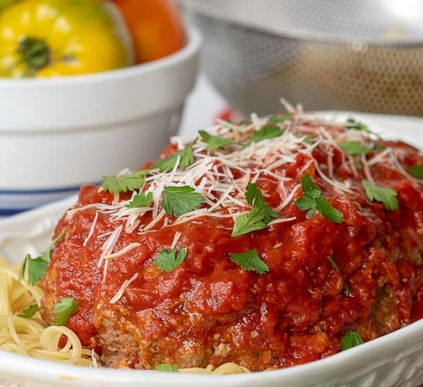 a large white serving dish with Italian meatloaf served on a bed of spaghetti