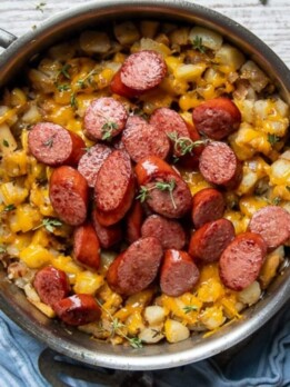 overhead shot of smoked sausage slices in a skillet over potato hash with cheese
