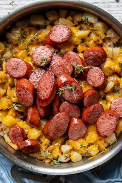 overhead shot of smoked sausage slices in a skillet over potato hash with cheese