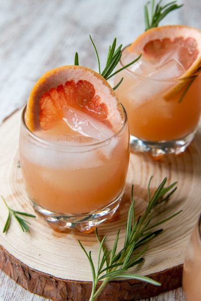two glasses of grapefruit vodka cocktails with fresh rosemary laying next to it