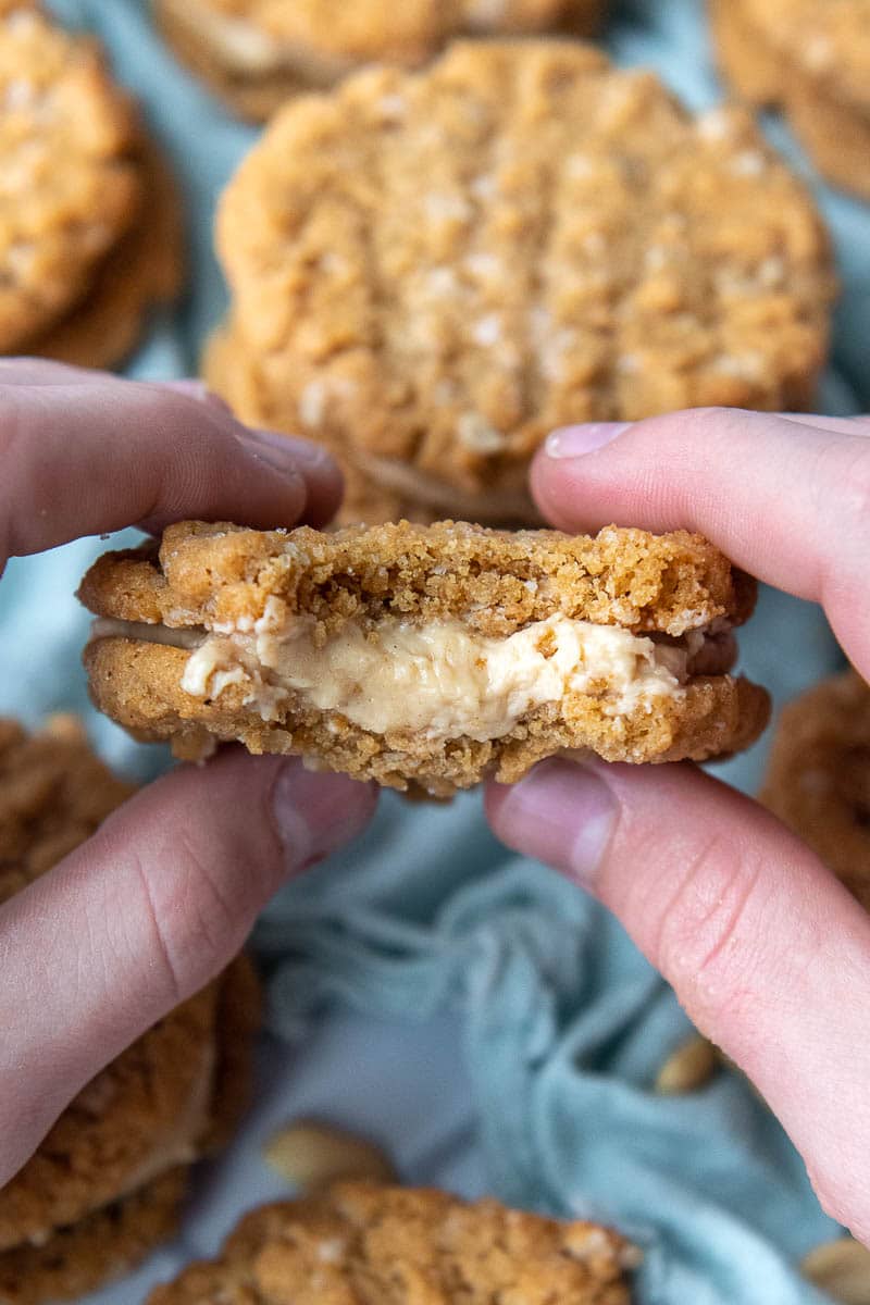 two hands holding up a peanut butter sandwich cookie with a bite taken out