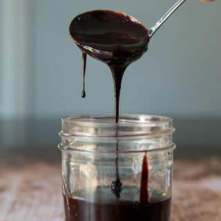 a ladle scooping in hot fudge sauce into a glass jar