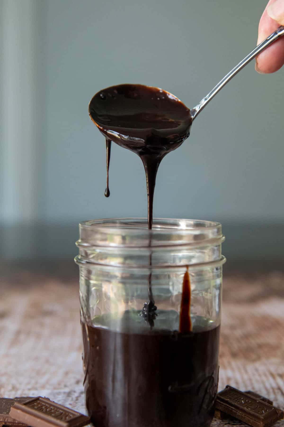 a ladle scooping in hot fudge sauce into a glass jar