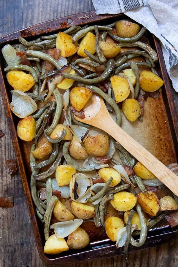 overhead shot of a baking sheet with roasted potatoes and green beans with a wooden spoon resting on it