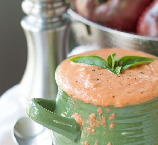 a bowl of cream of tomato soup dripping over the side with fresh basil floating on top