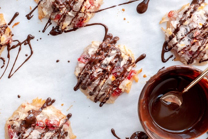 an overhead shot of cherry coconut macaroons on a baking sheet with a bowl of melted chocolate nearby
