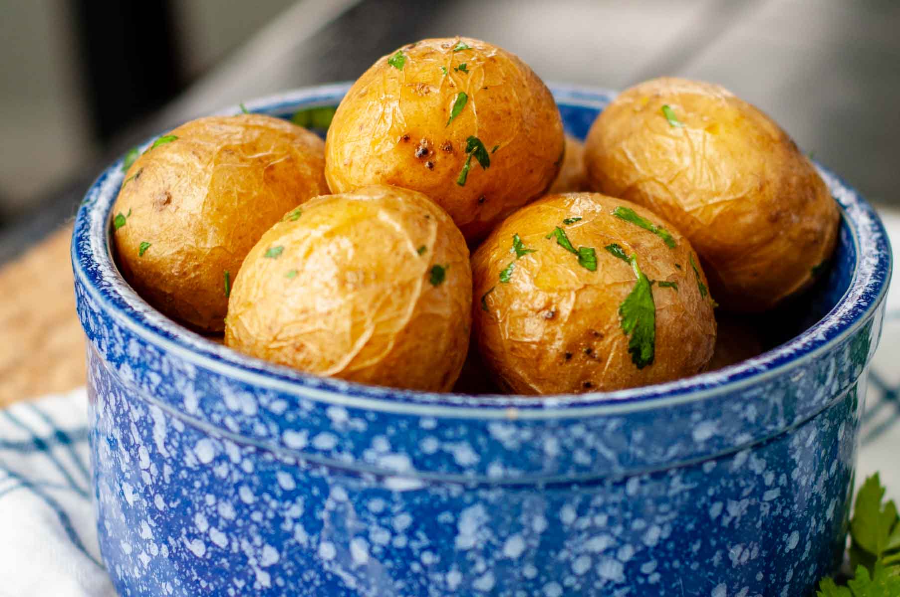 a pile of potatoes in a blue bowl with parsley sprinkled on top