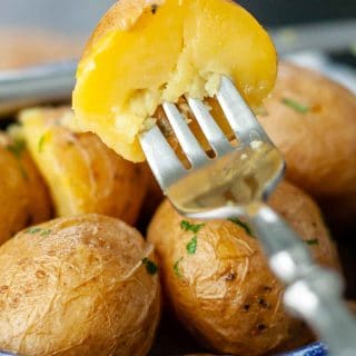 a fork lifting up half a potato from a blue bowl