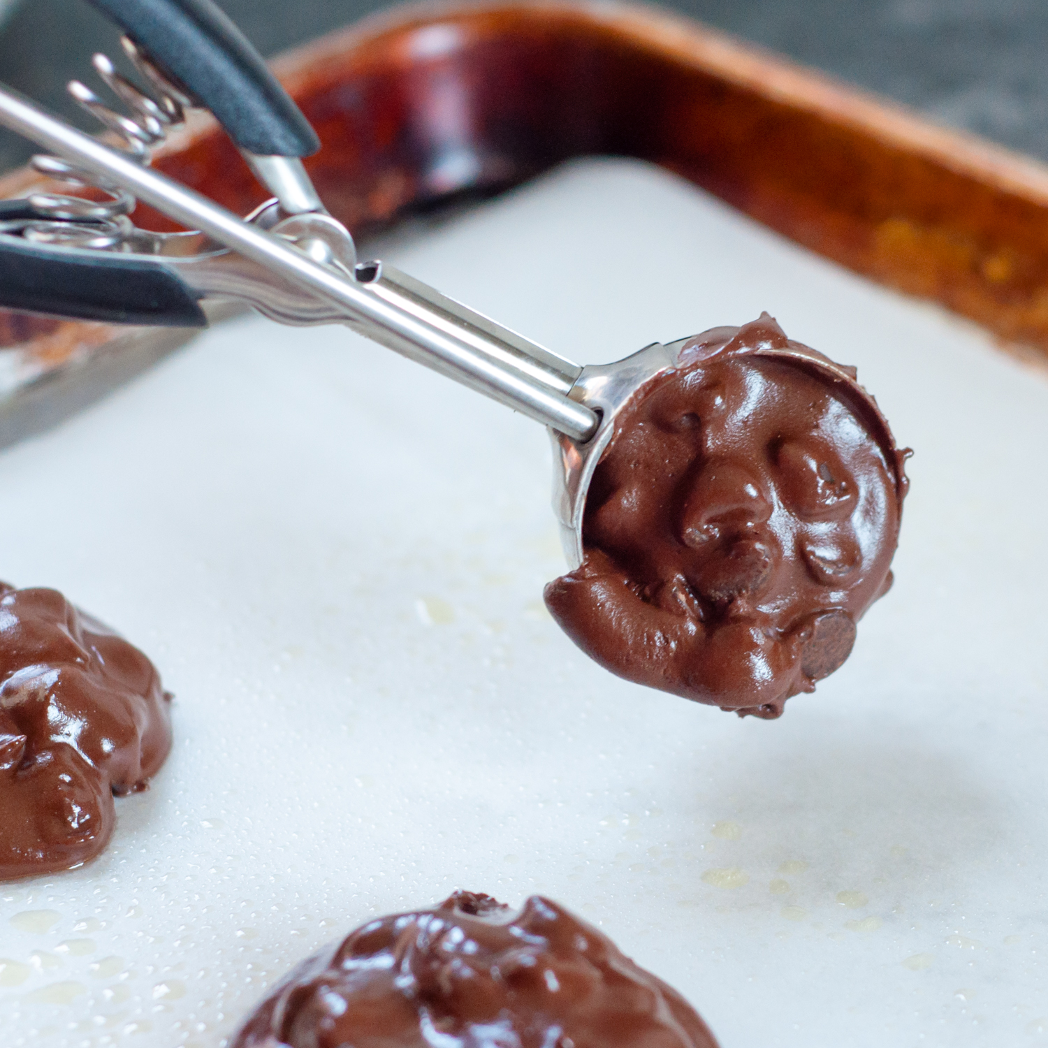 cookie scoop placing batter on a baking sheet.