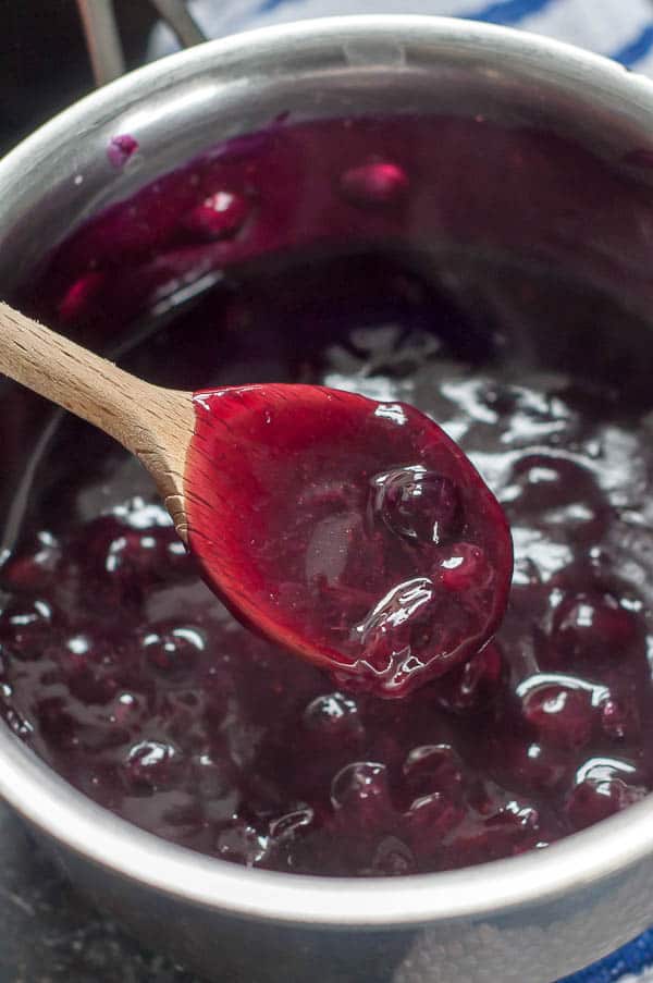 a wooden spoon holding up blueberry syrup from saucepan 
