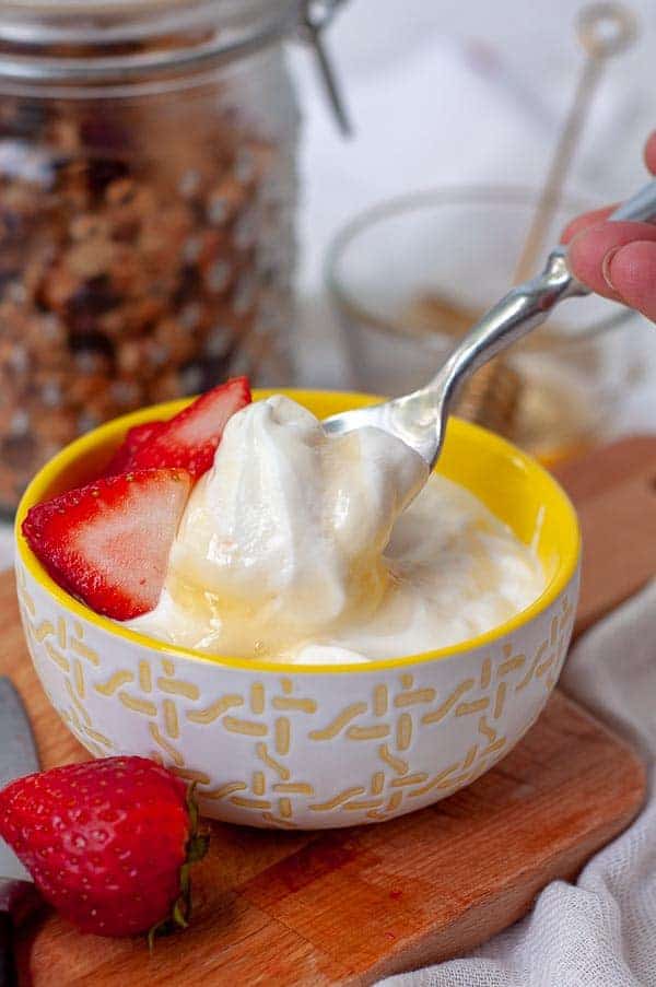 a spoon going into a bowl of homemade yogurt with honey drizzled on top