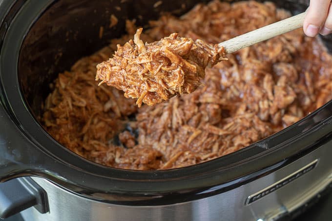 a wooden spoon holding up BBQ pulled chicken from a the slow cooker