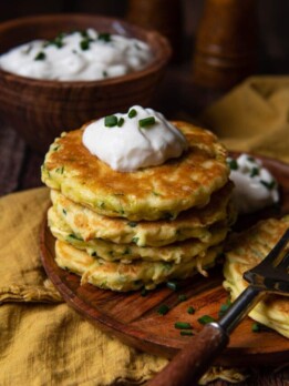 stack of zucchini fritters on a wood plate with a gold napkin underneath