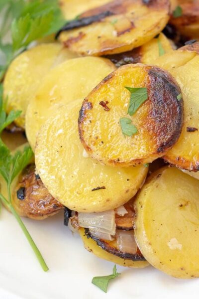 a close up of grilled potatoes on a white plate garnished with parsley
