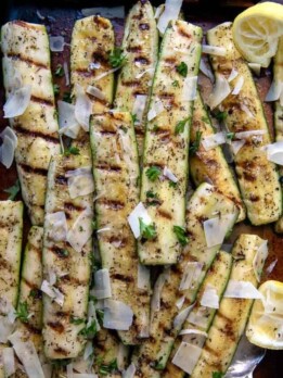 overhead shot of grilled zucchini and squash on a sheet pan with a serving utensil underneath