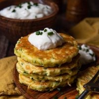 stack of zucchini fritters on a wood plate with a gold napkin underneath