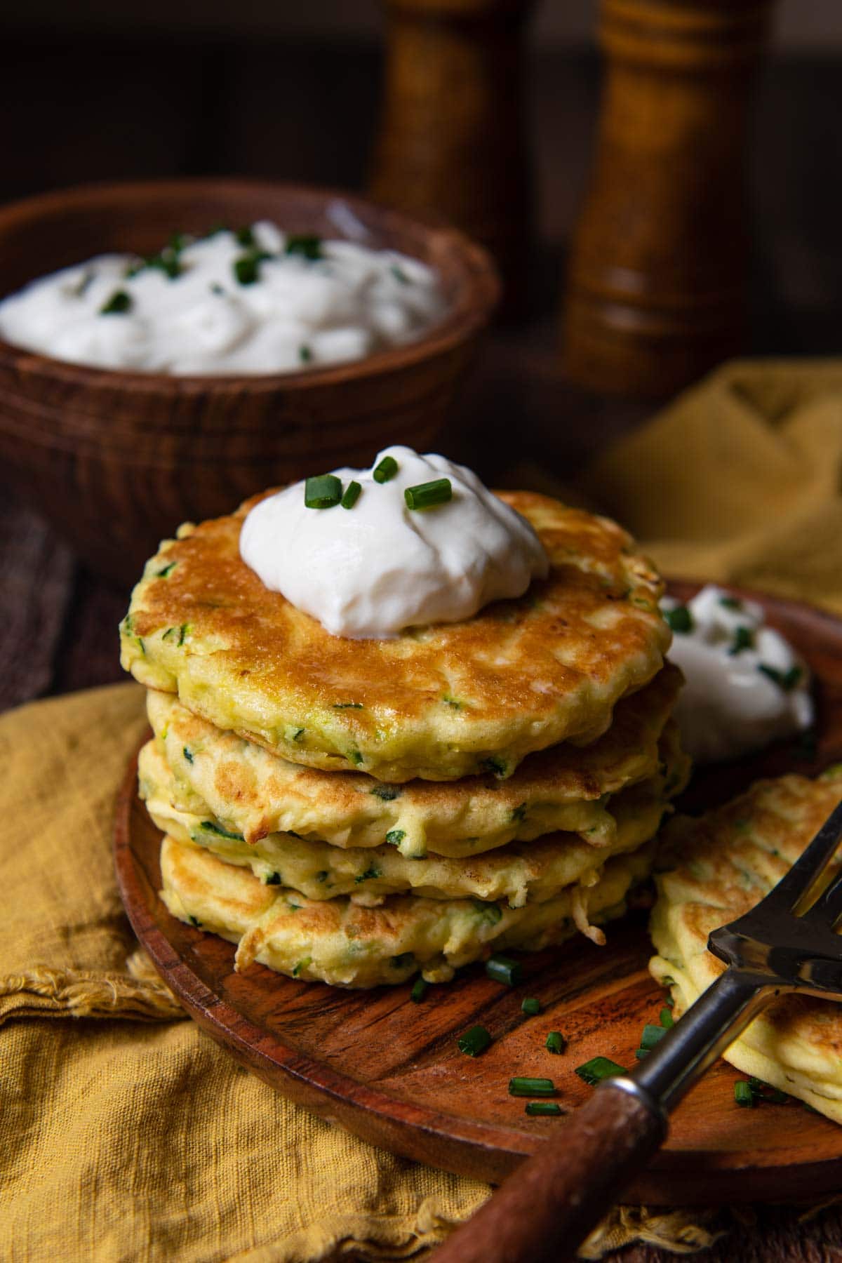 stack of zucchini fritters on a wood plate with a gold napkin underneath