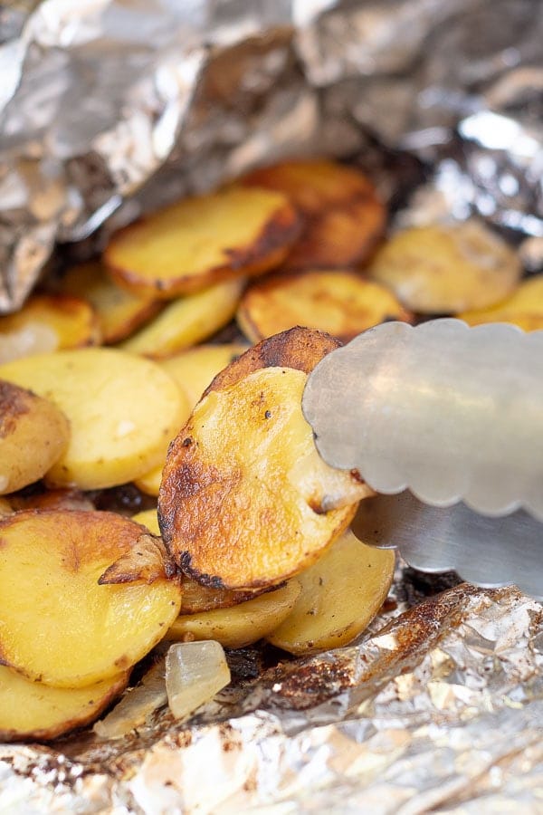 a tong picking up a grilled potato from foil