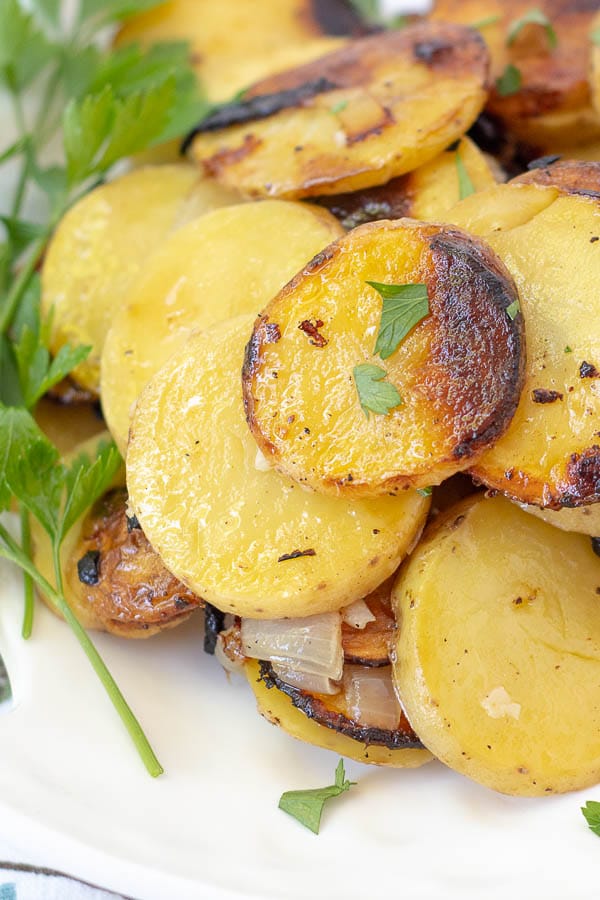 a close up of grilled potatoes on a white plate garnished with parsley