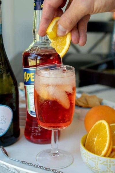 a fresh orange slice being squeezed into an Aperol spritz