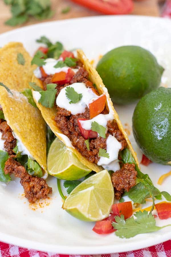 two tacos on a white plate with a couple limes resting next to it