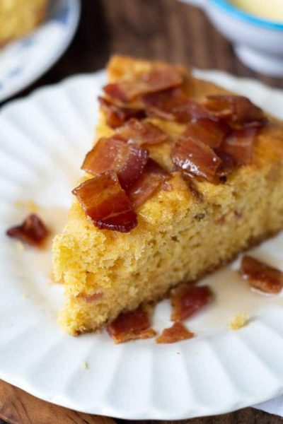 a wedge of bacon maple cornbread on a white plate with syrup drizzled over