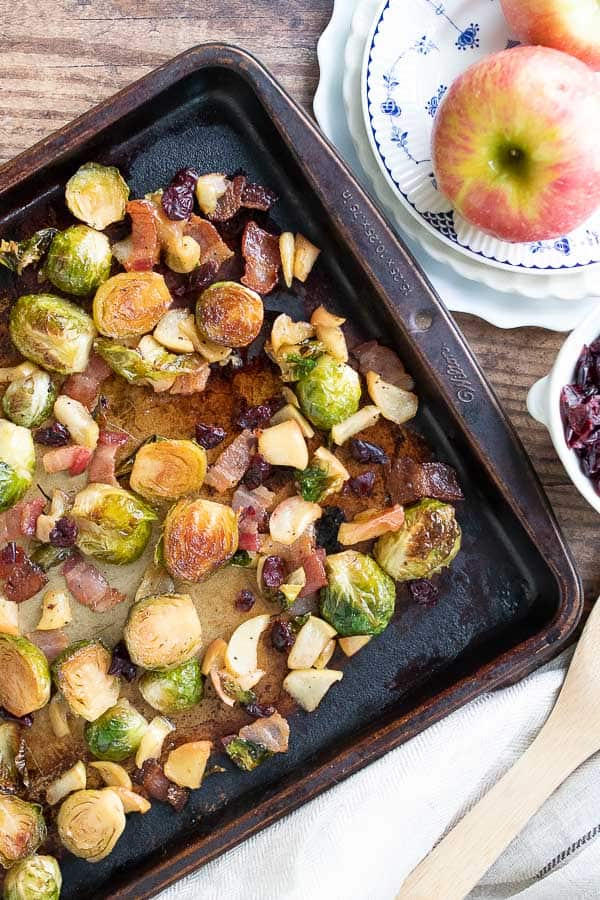 an overhead shot of a sheet pan with bacon roasted Brussels sprouts and apples laying next to it