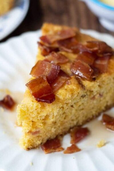 a wedge of bacon maple cornbread on a white plate with syrup drizzled over