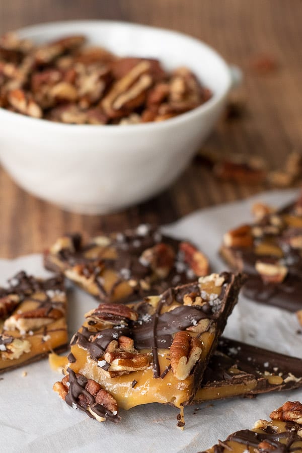 pieces of salted caramel chocolate bark on parchment with a bowl of pecans in background