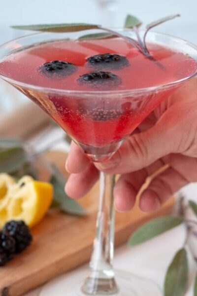 a hand about to lift up a martini glass filled with a blackberry martini