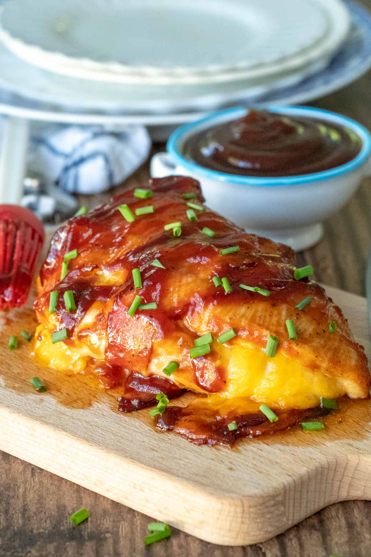 a chicken breast on a wooden cutting board stuffed with cheese and wrapped in bbq bacon