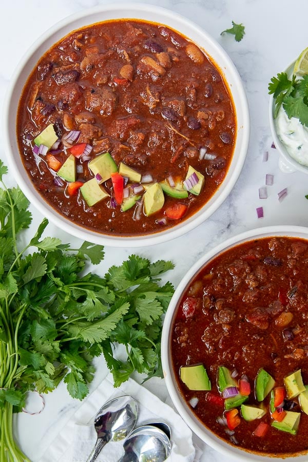overhead shot of two bowls of chorizo chili with avocados on top